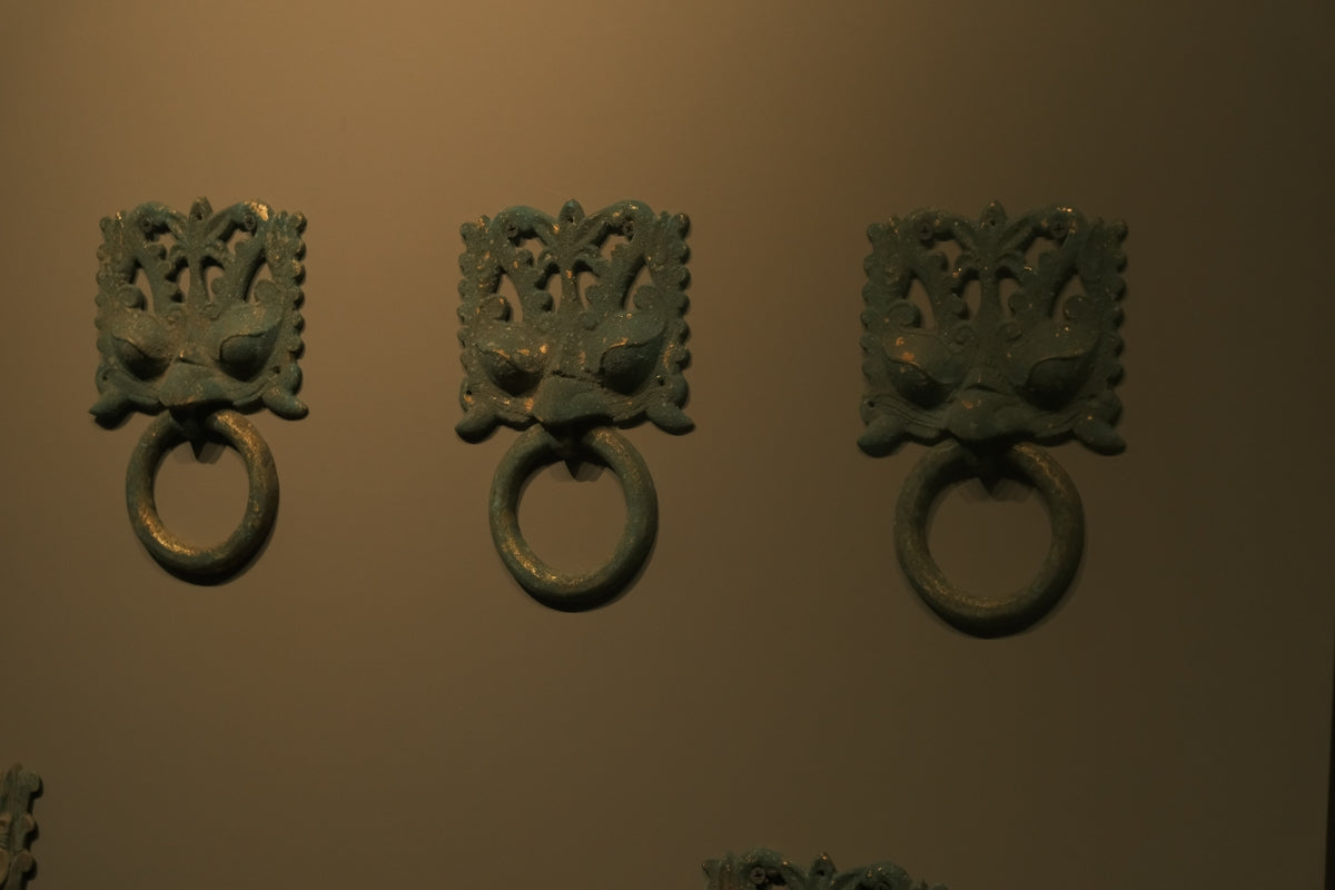 Three ornate dragon head door knockers on wall.