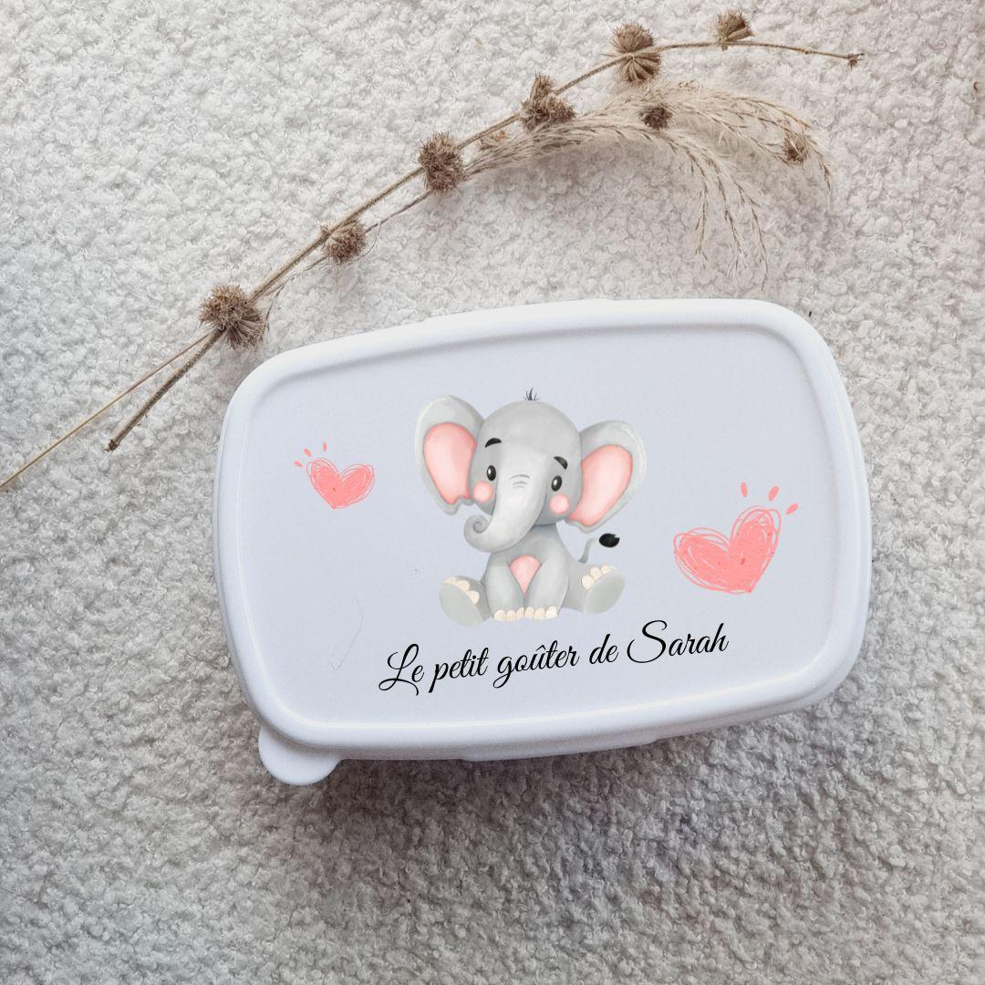 Kit de rentrée scolaire comprenant une boîte à lunch et une gourde assorties, personnalisées avec un prénom et des motifs colorés, posées sur une table en bois avec un fond lumineux.